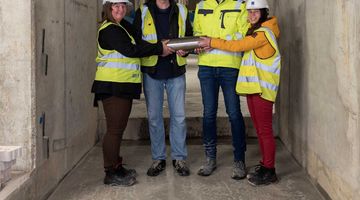 Prof. Kristian Franze, Dr. Dorothe Burggraf, Adrian Thoma and Katharina Kißner are gathered around the MPZPM time capsule before it is lowered into the concrete.